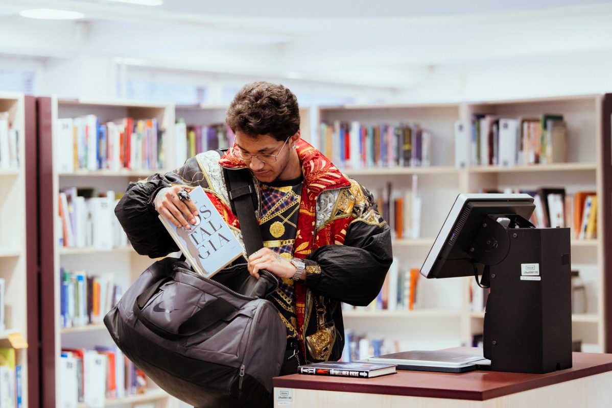 En kund med färgglad jacka packar upp böcker på sin väska i biblioteket.