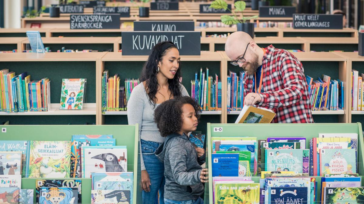 En vuxen och ett barn tittar på böcker som en bibliotekarie visar.