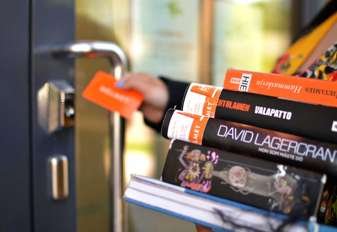 A customer with a stack of books and a library card outside a library.